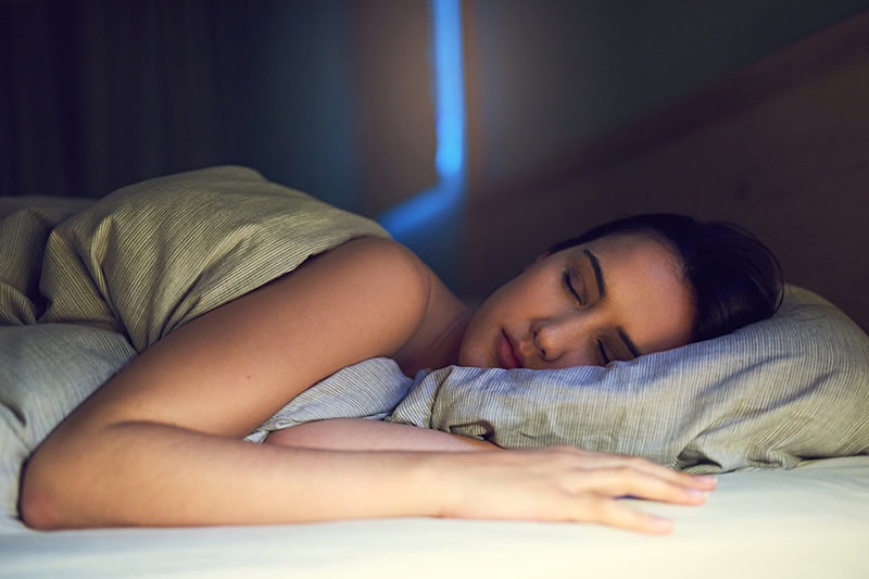 3 Health Benefits for Using Your AC While Sleeping. Young woman sleeping in her bed soundly.