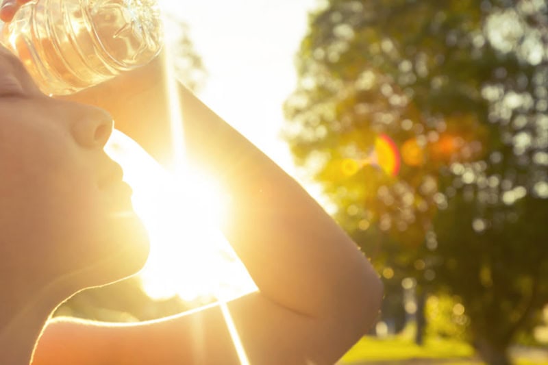3 Tips to Prevent an AC Breakdown During a Heat Wave. Woman using water bottle to cool down.